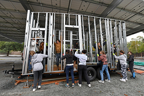 Carondelet High School students lift a wall into place and secure it to a trailer as they build a...