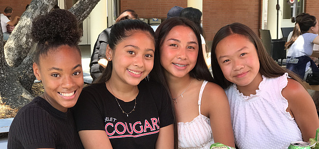 Four freshmen students sitting at a table smile at the camera at the Frosh Family Social on Augus...